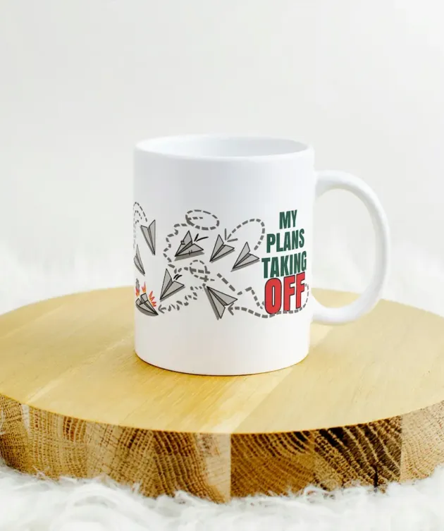 Cană „My Plans Taking OFF” așezată pe suport din lemn, cu design cu avioane de hârtie.