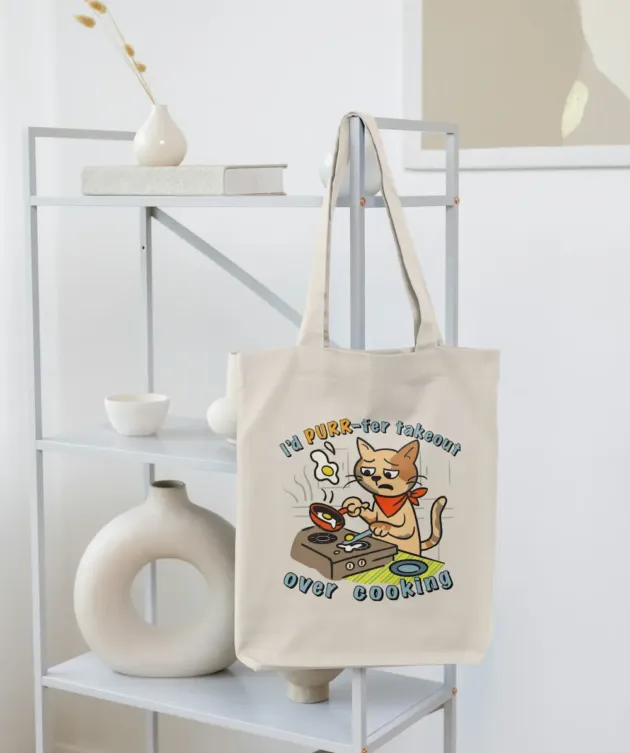 Geantă tote ecru cu print pisică la aragaz și textul „I’d PURR-fer takeout over cooking”, fotografiată pe suport.