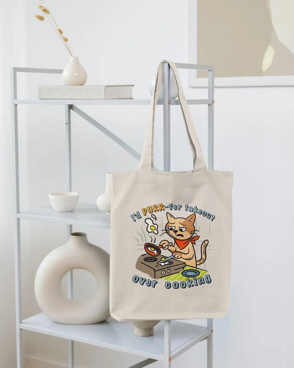 Geantă tote ecru cu print pisică la aragaz și textul „I’d PURR-fer takeout over cooking”, fotografiată pe suport.