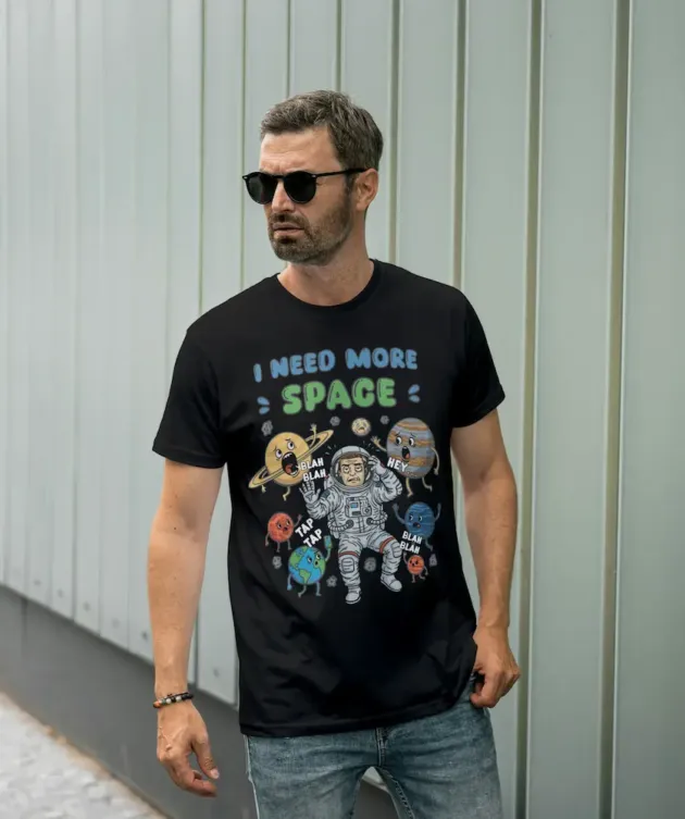 Bărbat purtând tricou negru cu design astronaut și text „I need more space”.